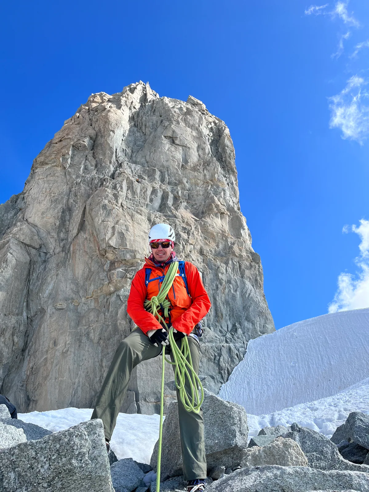 Joshua Ruoss en tenue d’alpinisme avec son casque et sa corde devant une aiguille rocheuse