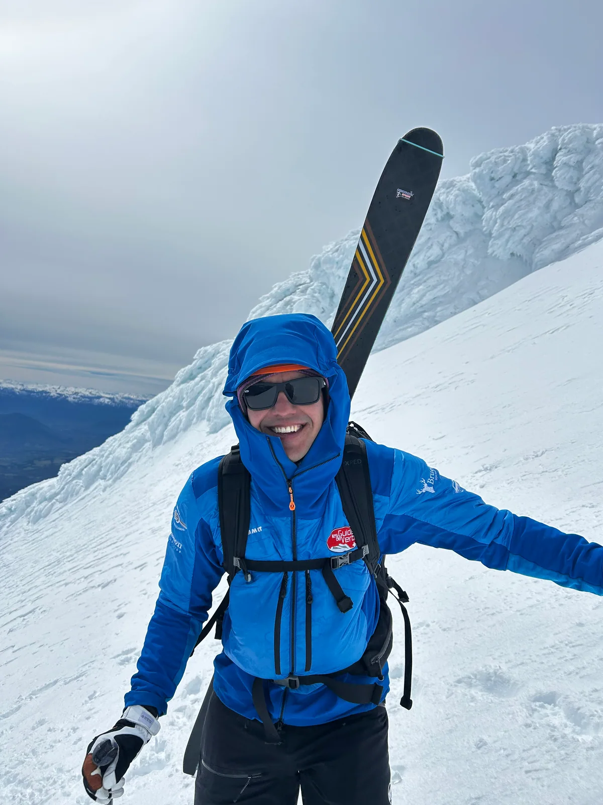 Joshua Ruoss souriant en montagne, en veste bleue et avec ses skis sur le sac