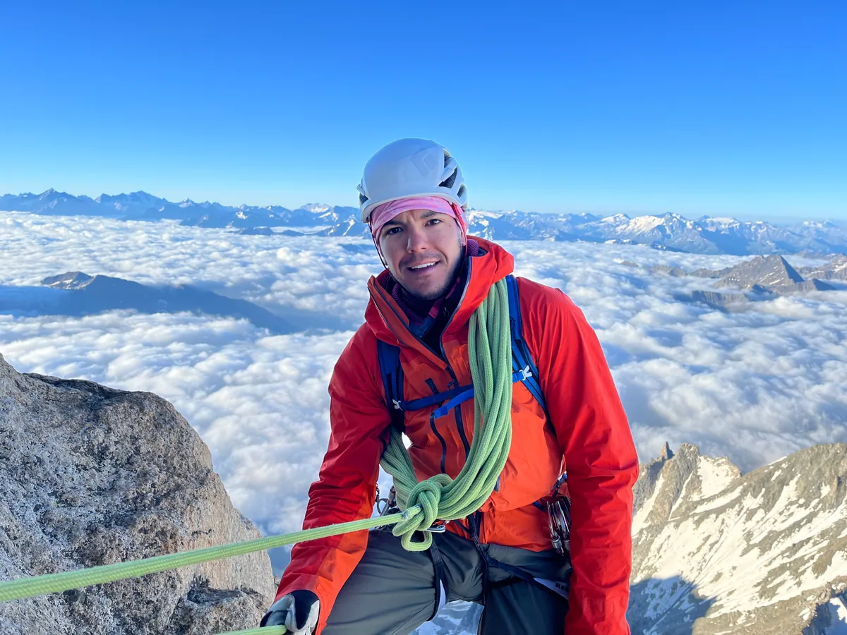 Josh souriant, avec son casque et sa corde, au-dessus d’une mer de nuages